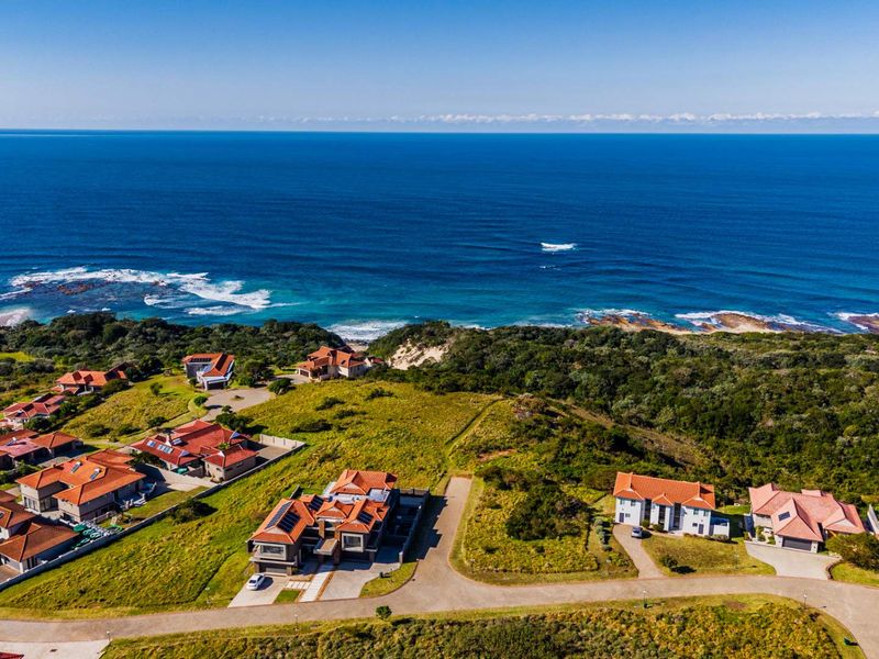 An aerial view of a coastal residential estate featuring multiple homes with tiled roofs, situated near the ocean with natural vegetation.