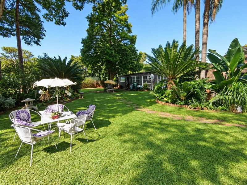 A well-maintained, lush green garden featuring mature trees, established tropical plants, and a stone pathway leading through the lawn.