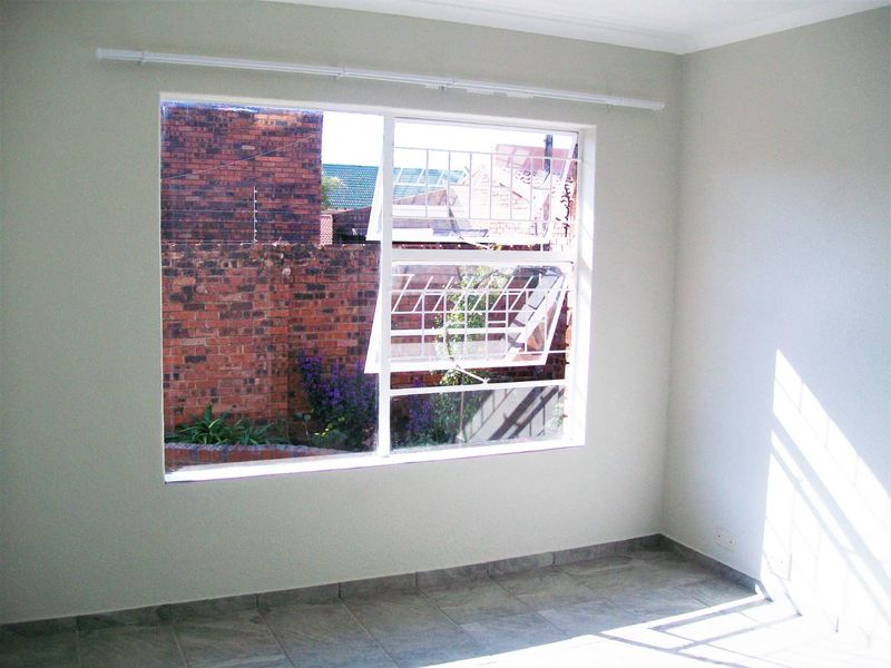 A bright, empty bedroom featuring tiled flooring, a large steel-framed window with security bars, and neutral wall finishes.