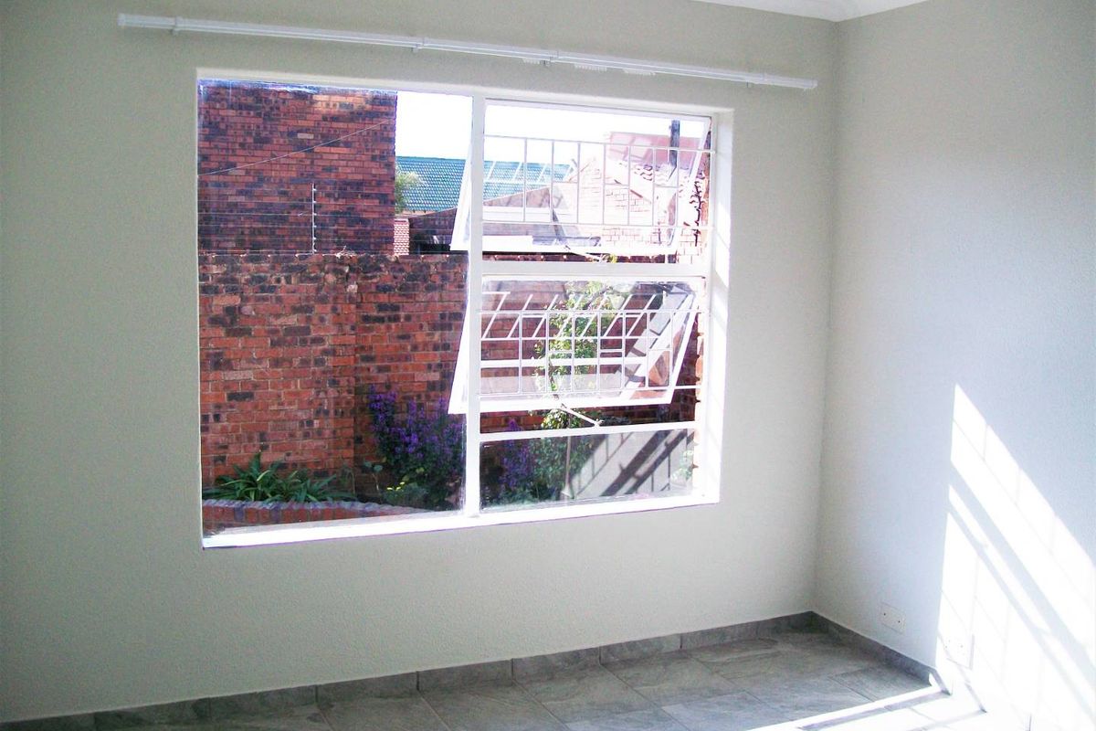A bright, empty bedroom featuring tiled flooring, a large steel-framed window with security bars, and neutral wall finishes.