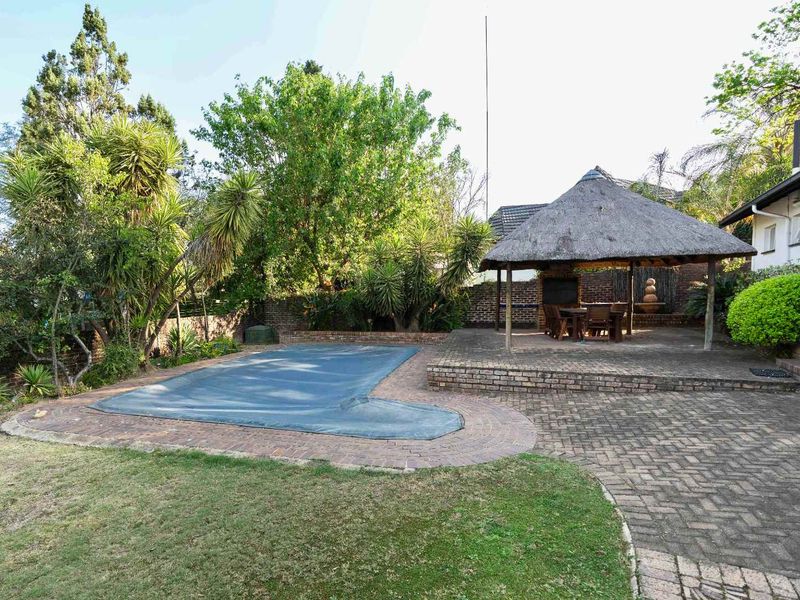 Outdoor entertainment area featuring a swimming pool with cover, brick-paved patio, and a traditional thatched lapa with a built-in braai.