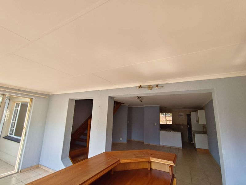 Open plan living area featuring a built-in wooden bar, tiled flooring, and a staircase leading to the upper level, with an adjacent kitchen space.
