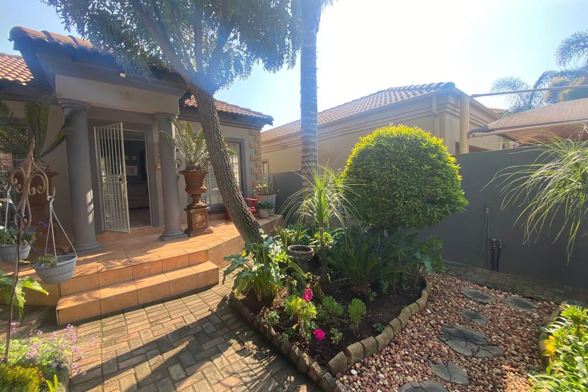 A well-maintained rear patio area featuring tiled flooring, decorative columns, and a landscaped garden with paved pathways and stone borders.