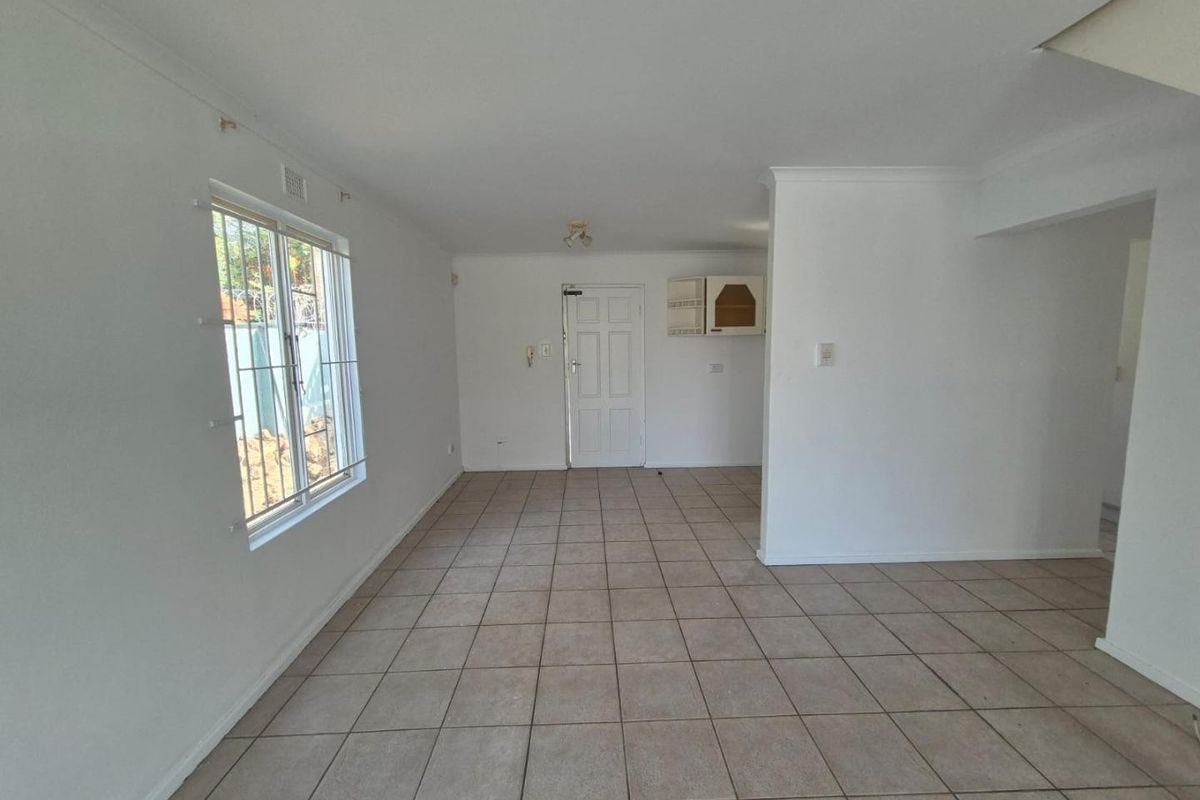 A bright, empty living area featuring neutral tiled flooring, coving, and a security-fitted window, offering a clean canvas for personalization.