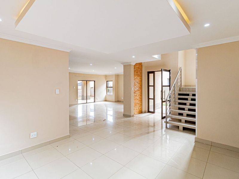 Spacious open-plan living area featuring polished porcelain tiles, a modern staircase with metal balustrades, and a decorative stone feature wall.