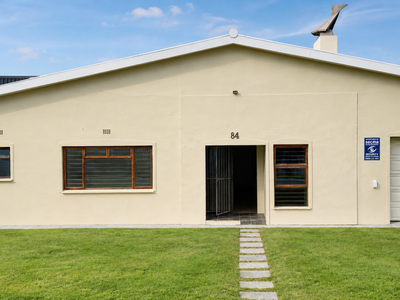 Front elevation of a single-story house featuring a garage, security gate, and a well-maintained lawn with a stone pathway.