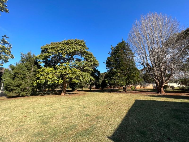 A spacious, well-maintained garden area featuring established mature trees and a large open lawn space.