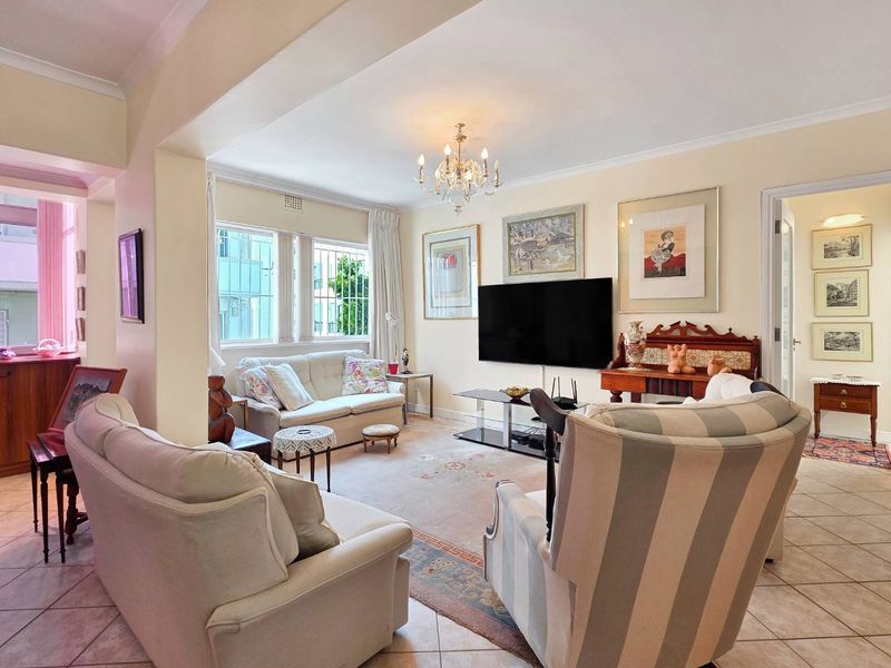 A spacious living room featuring tiled flooring, decorative cove cornicing, and large windows fitted with security bars, offering a bright and comfortable living space.