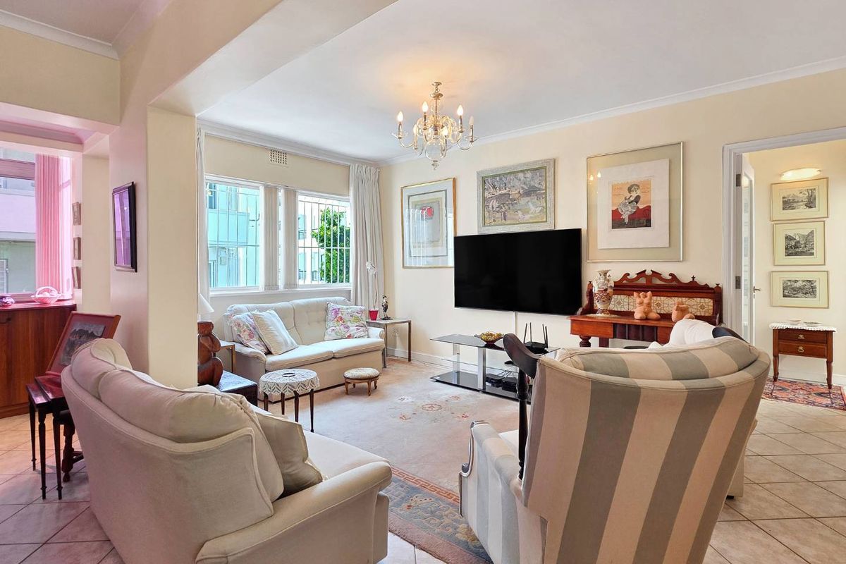 A spacious living room featuring tiled flooring, decorative cove cornicing, and large windows fitted with security bars, offering a bright and comfortable living space.
