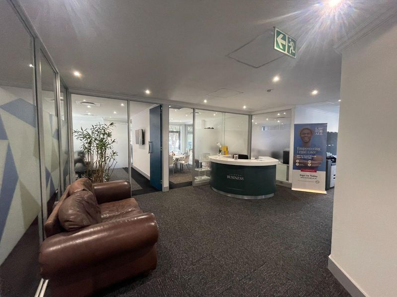 Professional office reception area featuring a curved reception desk, glass-partitioned offices, recessed lighting, and carpeted flooring.
