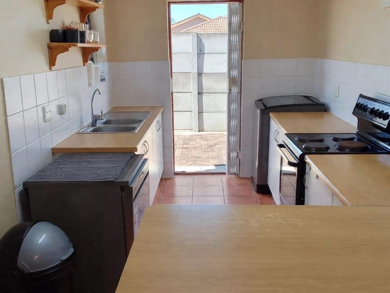 Functional kitchen featuring laminate countertops, double bowl sink, tiled splashback, and a freestanding stove with direct access to the rear exterior.