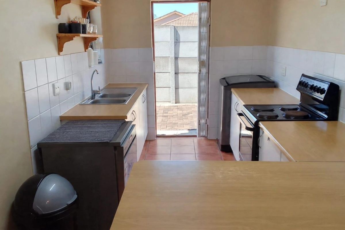 Functional kitchen featuring laminate countertops, double bowl sink, tiled splashback, and a freestanding stove with direct access to the rear exterior.