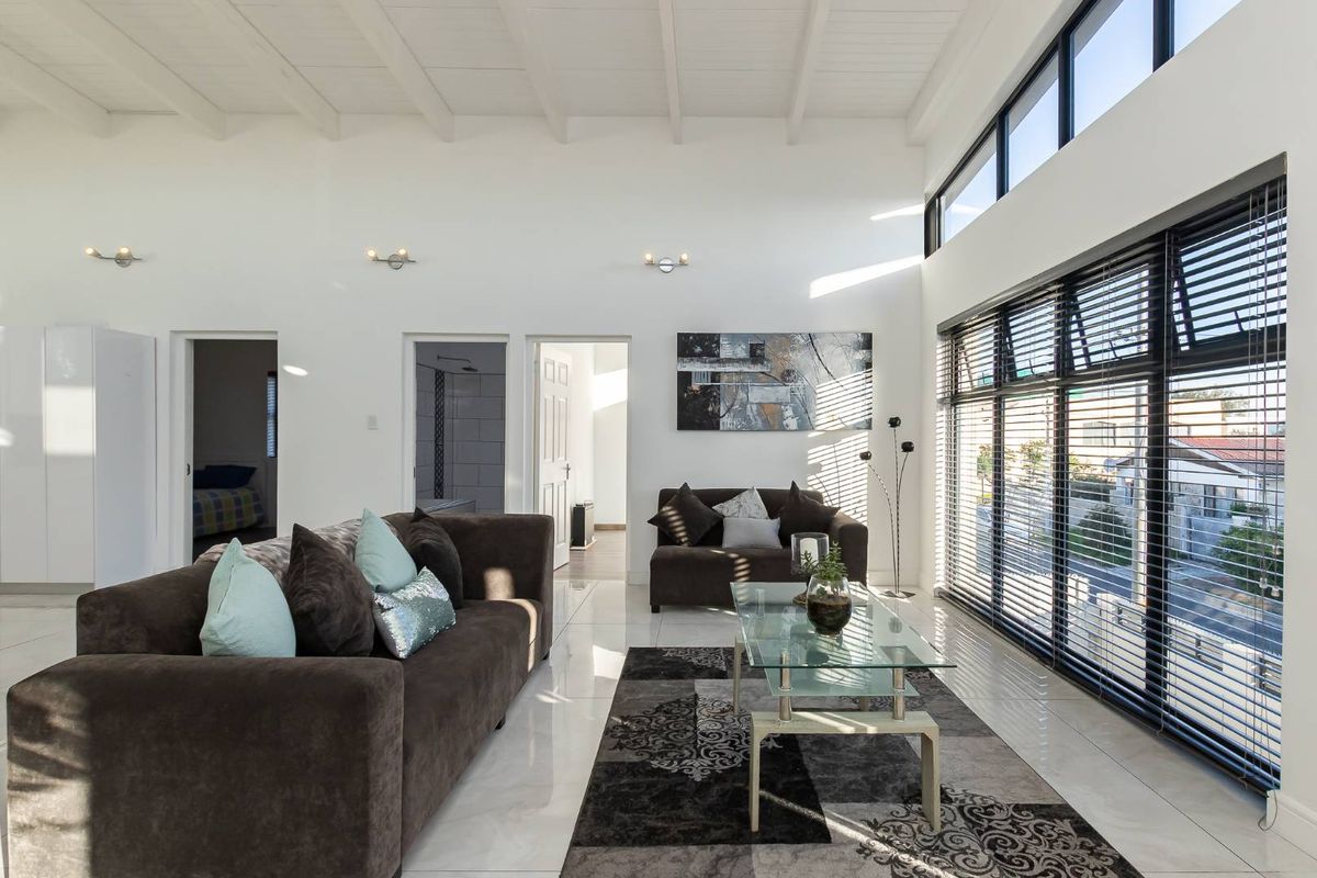 Spacious living room featuring high exposed beam ceilings, large format tiled flooring, and expansive windows with venetian blinds allowing for abundant natural light.