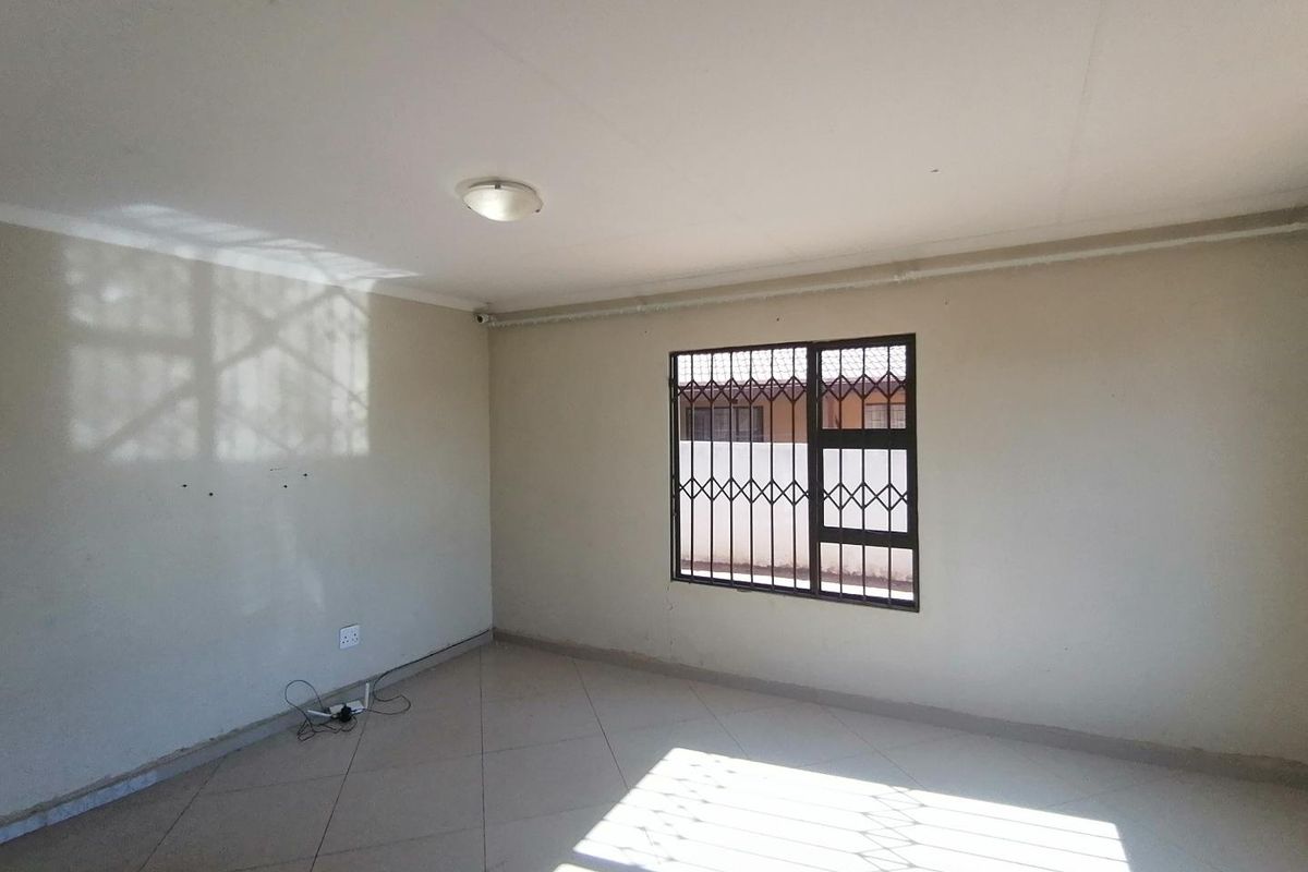 A vacant bedroom featuring tiled flooring, a window with security bars, and a ceiling-mounted light fixture.