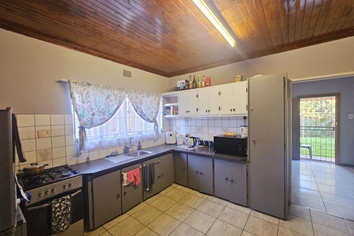 A functional kitchen featuring tiled flooring, wooden ceiling paneling, built-in cabinetry, and a freestanding gas stove with an integrated sink area.