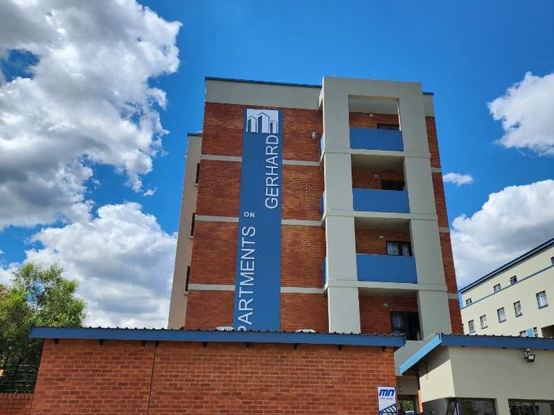 Exterior view of the Apartments on Gerhard building, featuring a brick facade, balconies, and a secure entrance gate with a guard house.