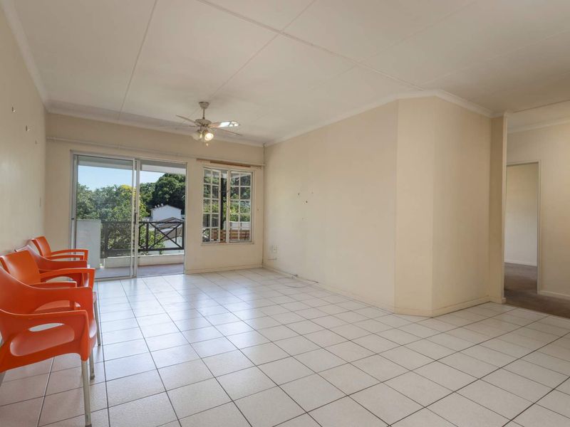 Spacious, light-filled living area featuring neutral tiled flooring, a ceiling fan, and direct access to an outdoor balcony through sliding glass doors.