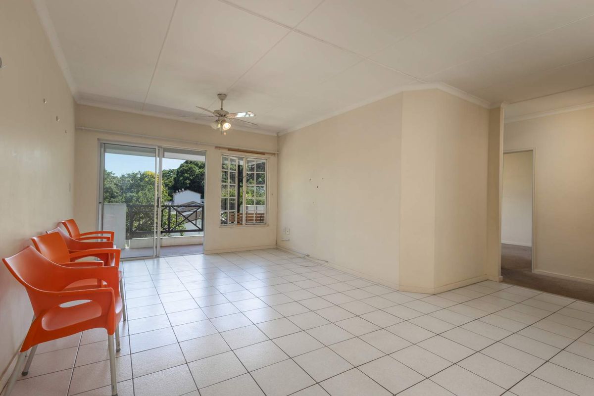 Spacious, light-filled living area featuring neutral tiled flooring, a ceiling fan, and direct access to an outdoor balcony through sliding glass doors.
