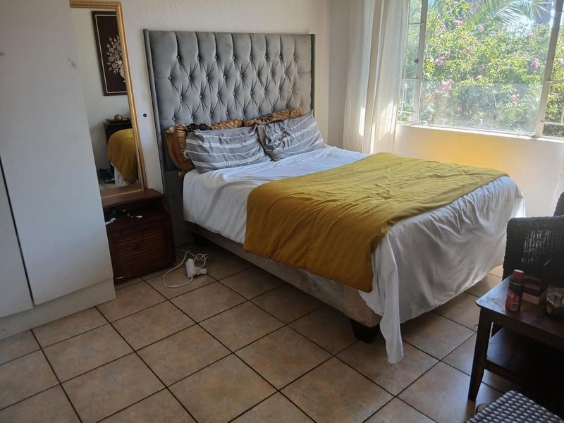 A bedroom featuring tiled flooring, a built-in wardrobe, and a large window providing natural light and garden views.