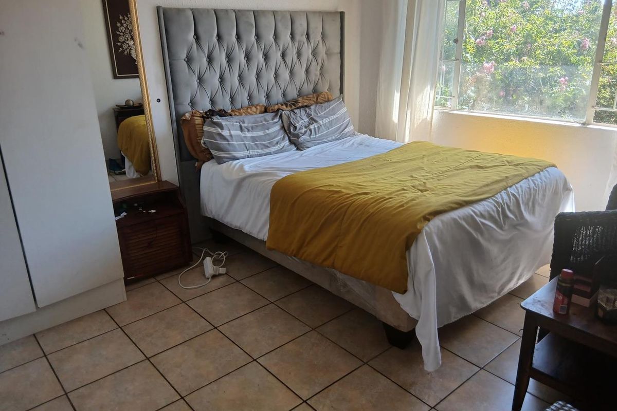 A bedroom featuring tiled flooring, a built-in wardrobe, and a large window providing natural light and garden views.