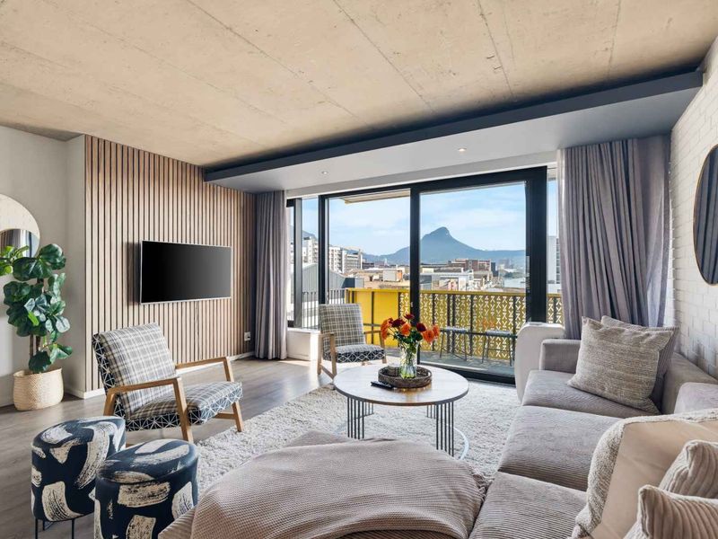 Modern living room featuring an exposed concrete ceiling, timber slat feature wall, and large sliding doors opening to a balcony with mountain views.