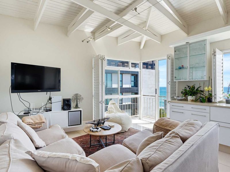 Bright living room featuring vaulted ceilings with exposed beams, built-in cabinetry, and bi-fold doors opening to a balcony with ocean views.