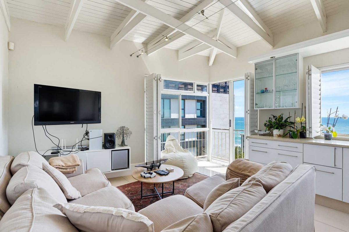 Bright living room featuring vaulted ceilings with exposed beams, built-in cabinetry, and bi-fold doors opening to a balcony with ocean views.