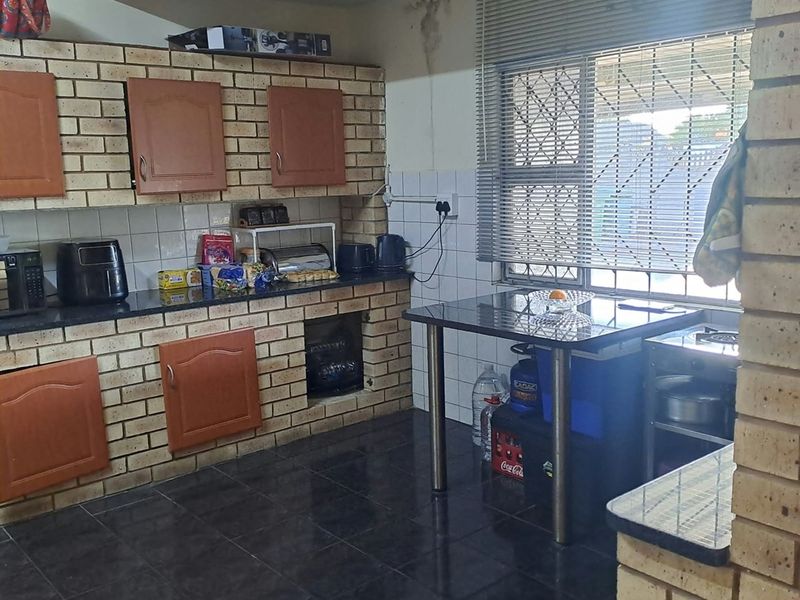 Kitchen featuring face brick cabinetry, dark tiled flooring, and a granite countertop, with a security gate and venetian blinds installed on the window.