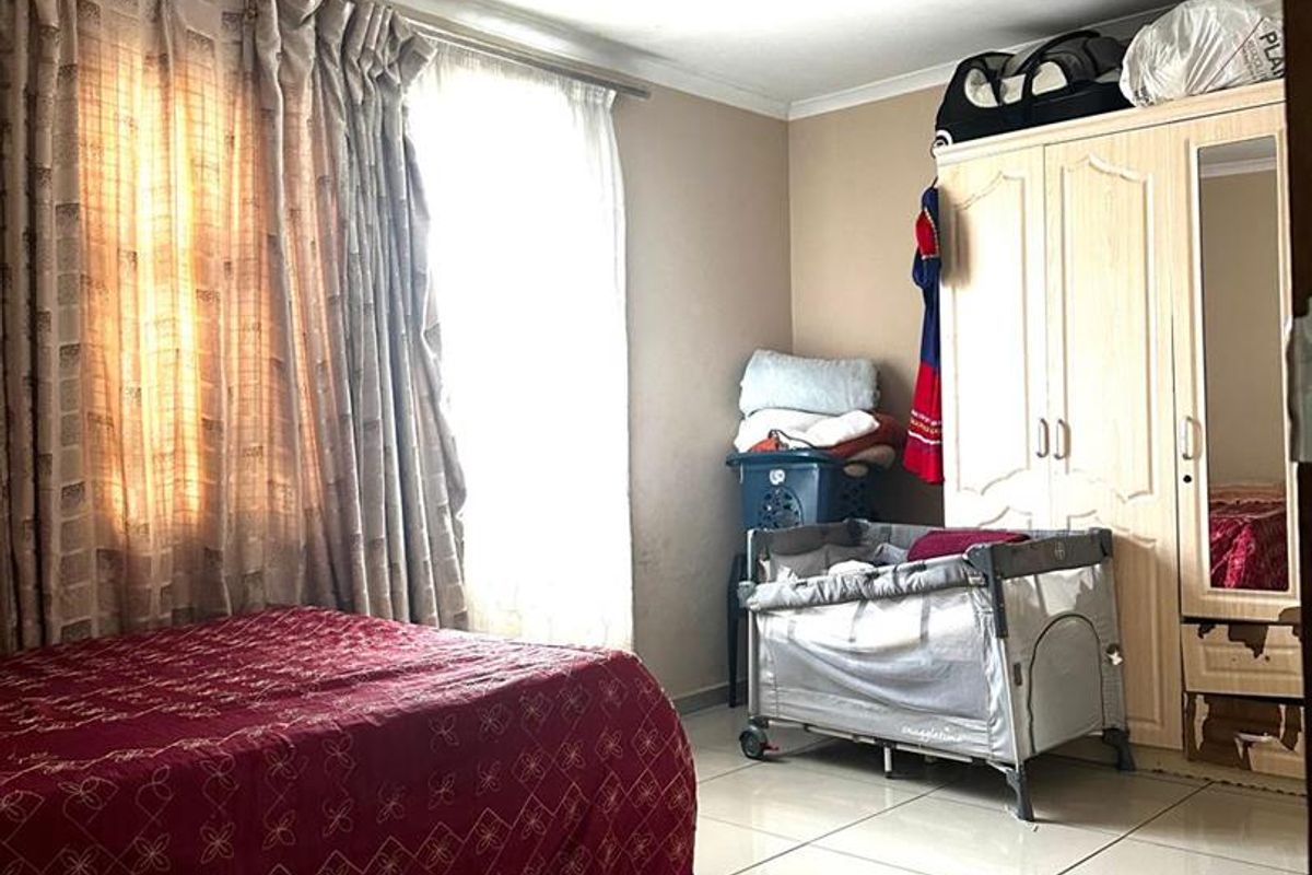 A bedroom featuring tiled flooring, a built-in wardrobe, and large windows with curtains, providing a functional living space.