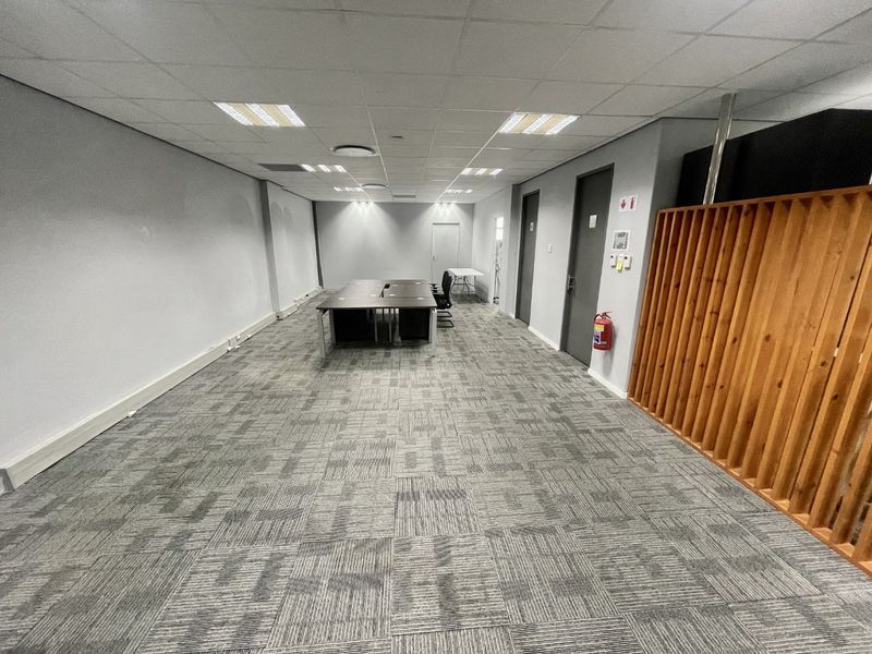 A functional office space featuring a suspended ceiling, recessed lighting, carpet tiles, and a decorative timber slat partition.