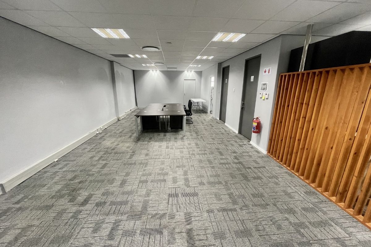 A functional office space featuring a suspended ceiling, recessed lighting, carpet tiles, and a decorative timber slat partition.