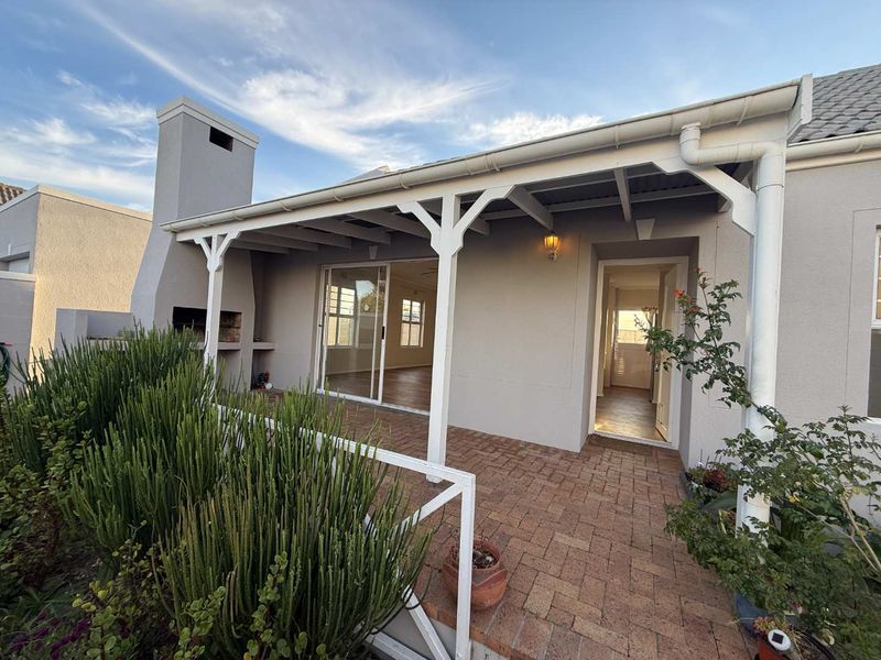 A well-maintained covered patio featuring brick paving and a built-in braai, providing seamless indoor-outdoor flow through sliding glass doors.