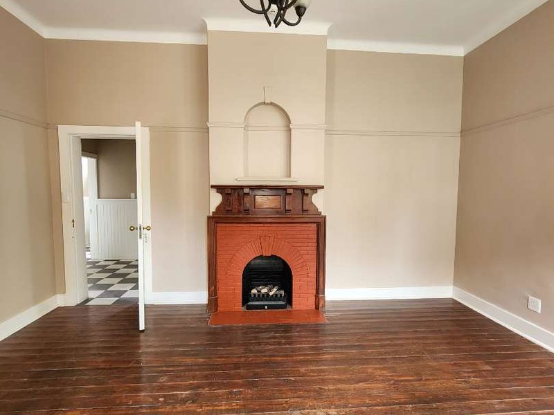 Spacious living room featuring original hardwood flooring, a classic brick fireplace with a timber mantelpiece, and traditional picture rails.