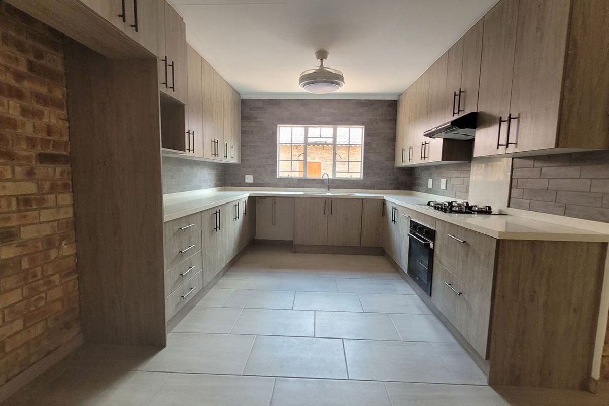 Modern kitchen featuring light wood-grain cabinetry, stone countertops, built-in oven, gas hob, and an attractive exposed brick feature wall.