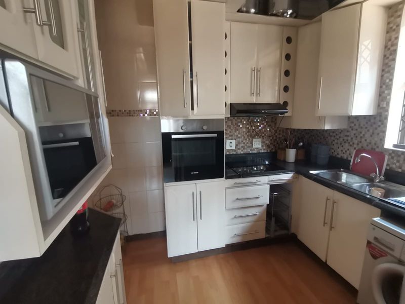 A functional kitchen featuring cream cabinetry, granite countertops, built-in oven, electric hob, and a tiled backsplash with laminate flooring.