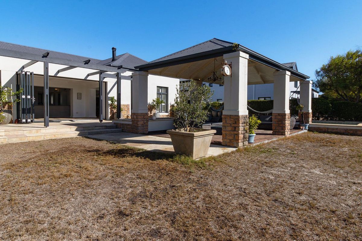 Spacious rear exterior featuring a covered patio area with stone pillars, bi-fold doors, and a paved terrace overlooking the garden.