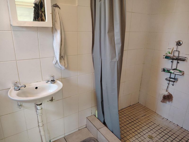 A functional bathroom featuring a wall-mounted basin, tiled shower enclosure, and basic sanitary fittings, requiring cosmetic updates to improve its overall condition.