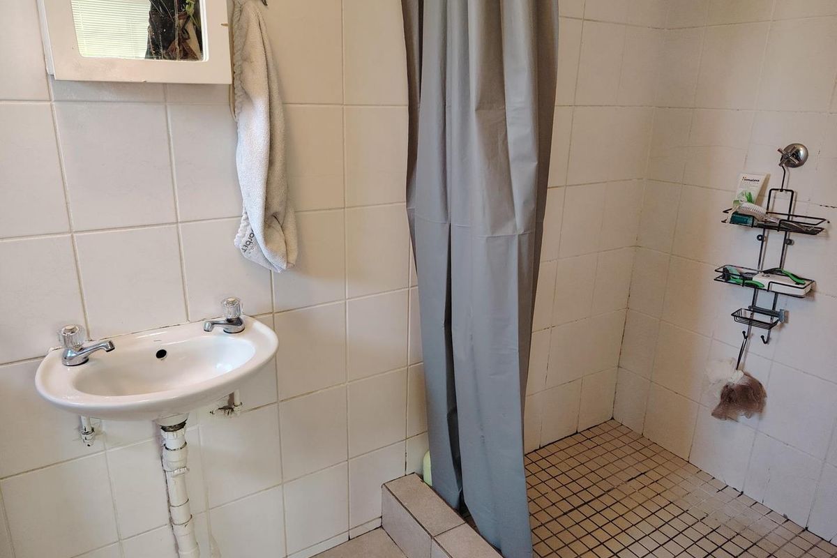 A functional bathroom featuring a wall-mounted basin, tiled shower enclosure, and basic sanitary fittings, requiring cosmetic updates to improve its overall condition.