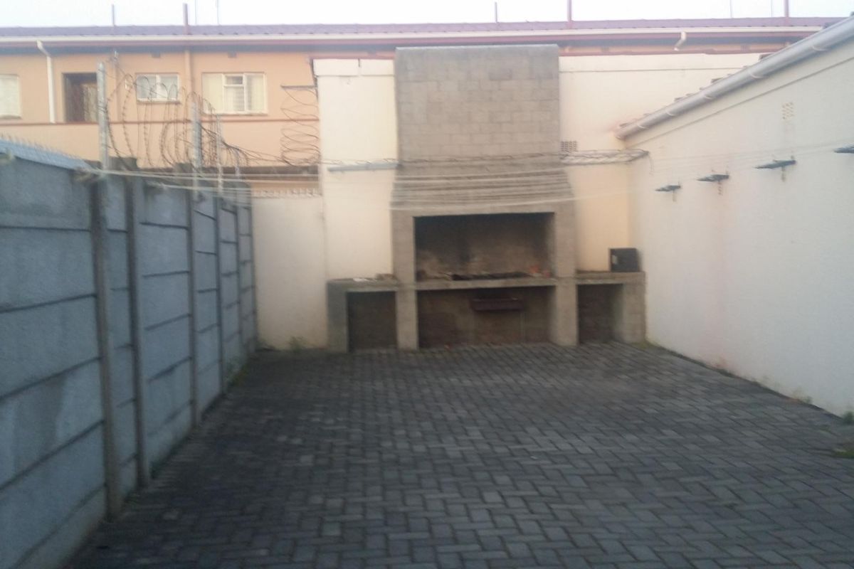 Rear courtyard area featuring a built-in brick braai, paved flooring, and enclosed by precast concrete boundary walls with security fencing.