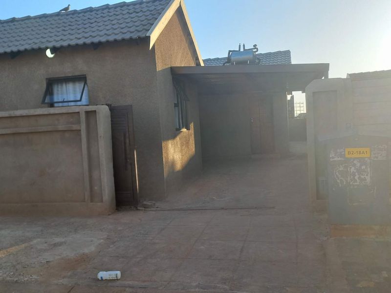 Front exterior view of the house featuring a paved driveway, carport, and boundary wall with a solar geyser installed on the roof.