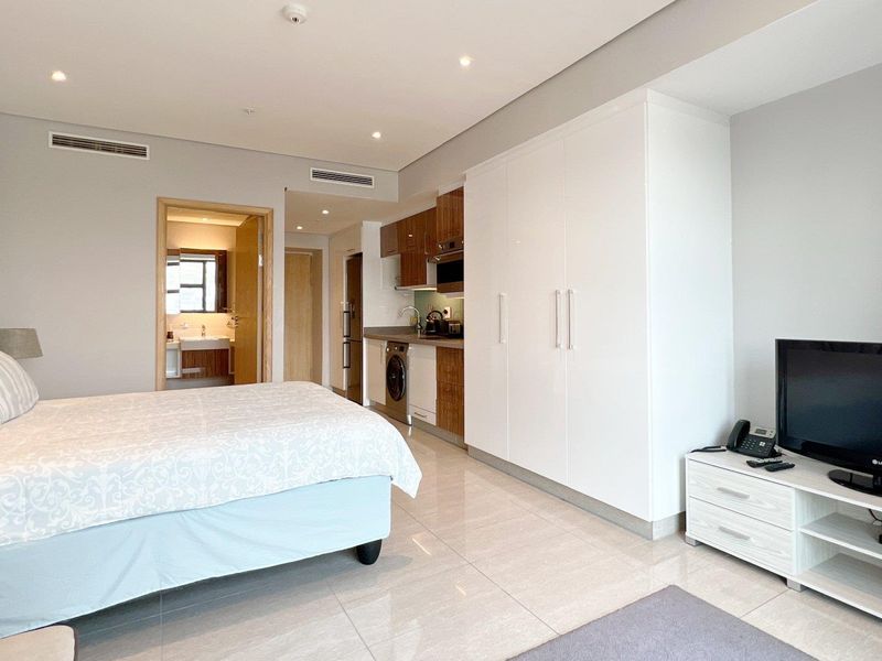 Modern open-plan studio apartment featuring a compact kitchenette, built-in storage, tiled flooring, and ducted air conditioning with an en-suite bathroom.