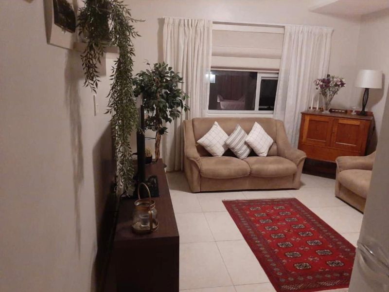 A cozy living room featuring neutral tiled flooring and a large window with curtain treatments, providing a comfortable and functional space.