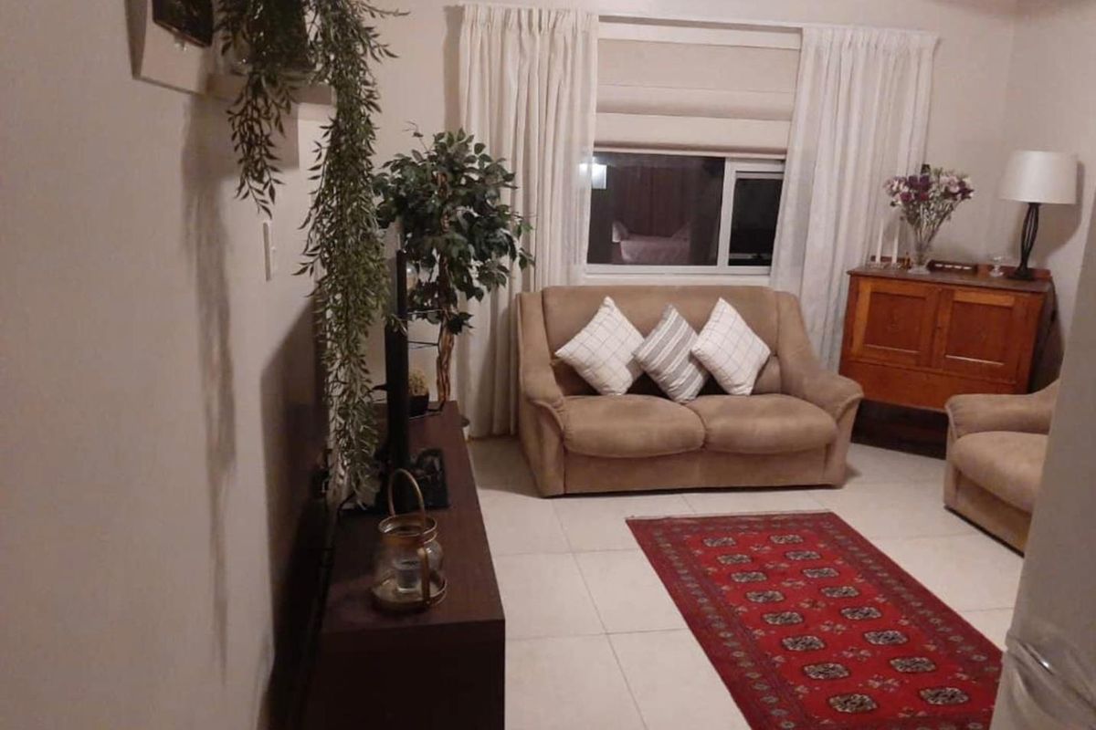 A cozy living room featuring neutral tiled flooring and a large window with curtain treatments, providing a comfortable and functional space.