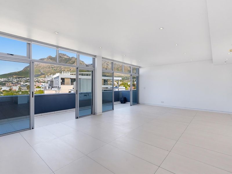 Spacious, light-filled living area featuring large format floor tiles, recessed lighting, and expansive sliding glass doors opening onto a balcony with mountain views.