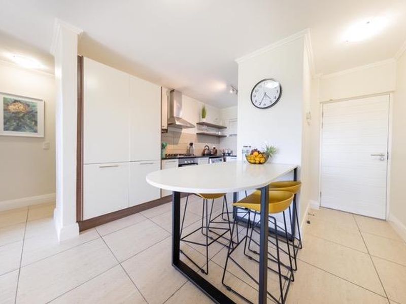 Modern kitchen featuring sleek white cabinetry, stone countertops, a breakfast bar, and integrated appliances, finished with neutral ceramic floor tiles.