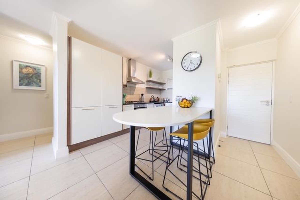 Modern kitchen featuring sleek white cabinetry, stone countertops, a breakfast bar, and integrated appliances, finished with neutral ceramic floor tiles.