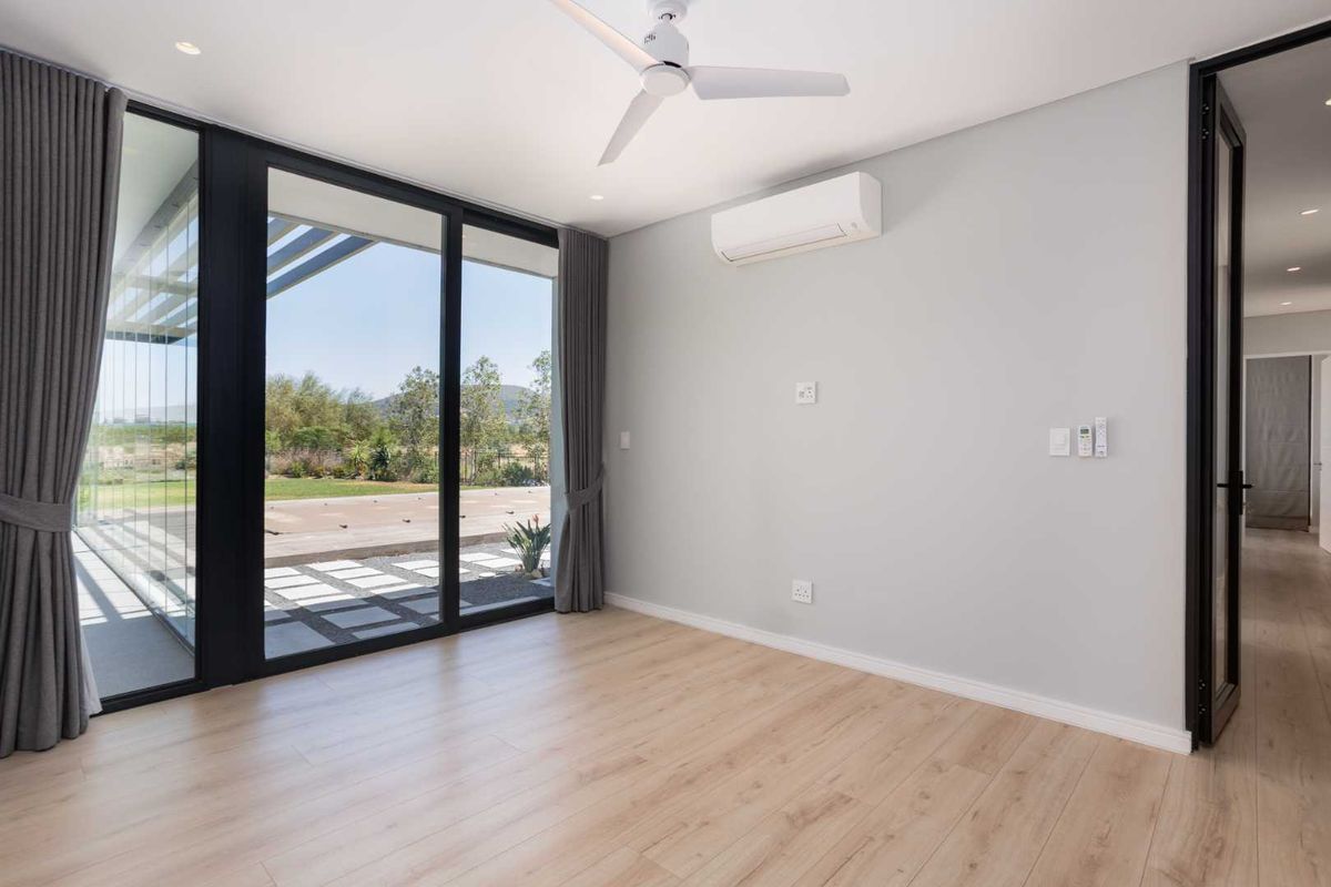 A bright, modern bedroom featuring laminate flooring, a ceiling fan, split-system air conditioning, and large sliding glass doors leading to an outdoor area.