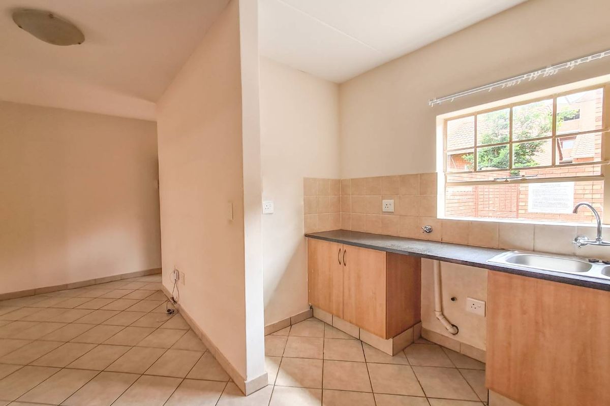 A functional kitchen area featuring tiled flooring, laminate cabinetry, a stainless steel sink, and a tiled splashback, offering a blank canvas for updates.
