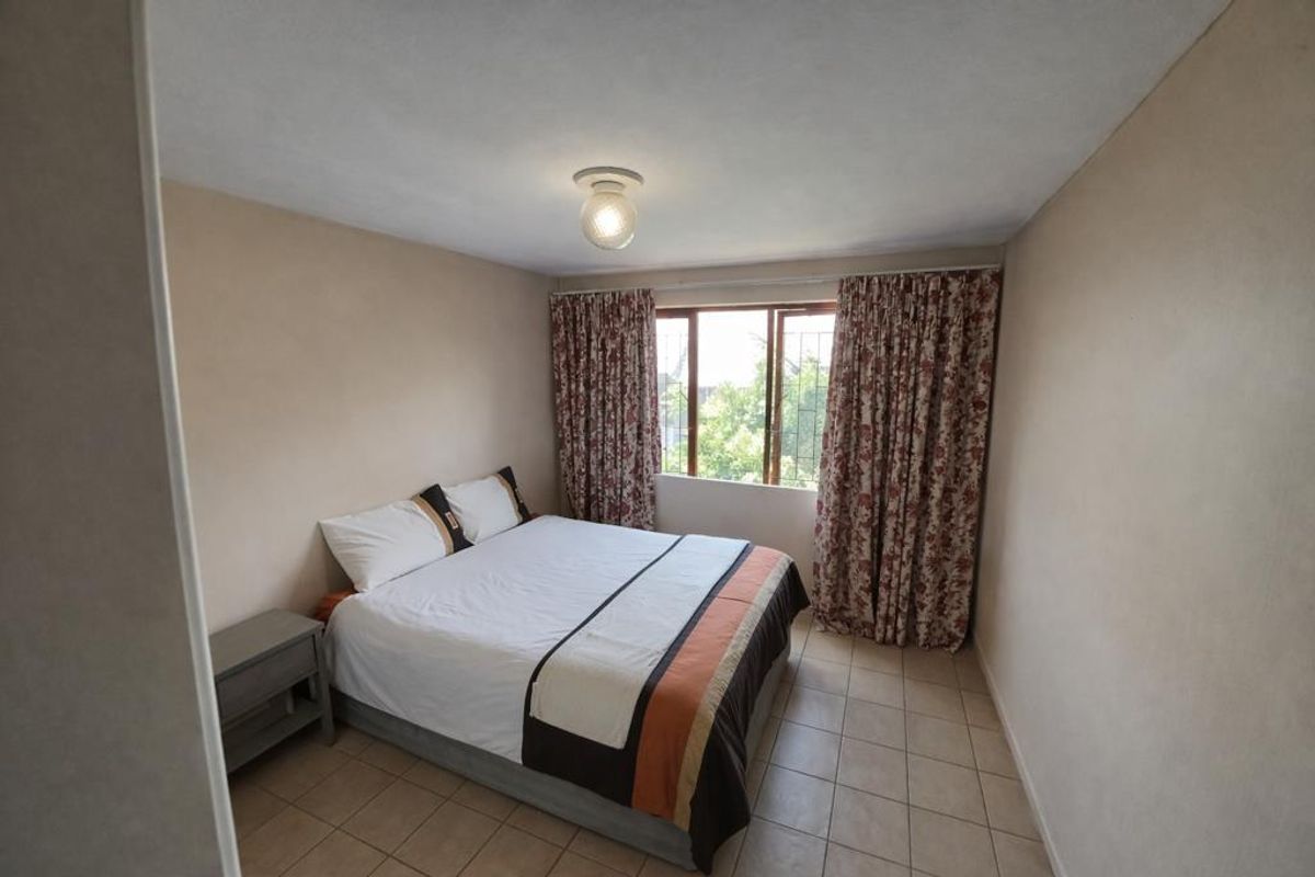 A functional bedroom featuring tiled flooring, a window with security bars, and a central light fixture.