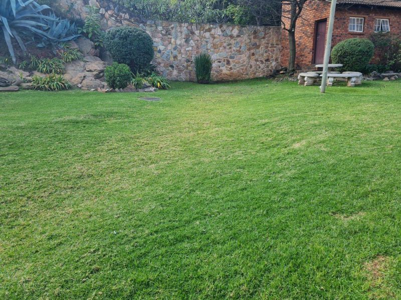 A well-maintained private garden featuring a lush lawn, established rockery, and a decorative stone boundary wall.